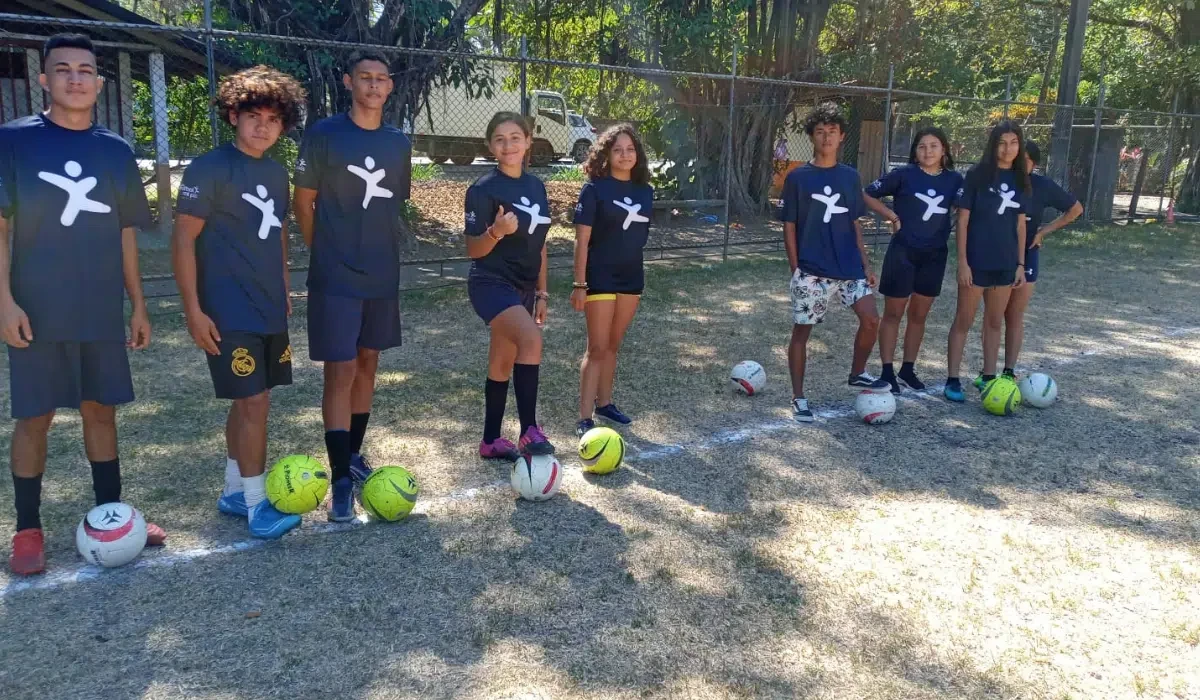 Children from the Fútbol por mi País youth program posing with soccer balls on a dirt court in Santa Teresa