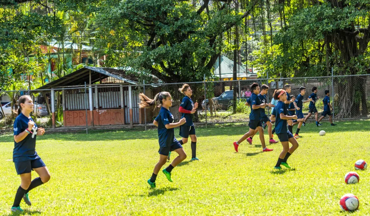 Youth players in Fútbol por mi País jerseys running drills on a grass field in Santa Teresa, Costa Rica